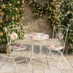 Conjunto de jardín compuesto por mesa redonda y dos sillas plegables de estructura metálica negra con asiento y tablero de mosaico decorativo, ideal para terraza o patio exterior.