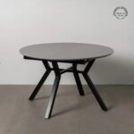 Mesa extensible redonda con patas de metal negro y tablero cerámico gris.