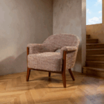 Sillón tapizado beige-marrón con estructura de madera sobre suelo de parquet y fondo neutro