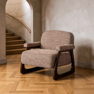Sillón tapizado beige-marrón con estructura de madera oscura sobre suelo de parquet y fondo neutro