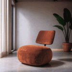 Sillón bajo color terracota tapizado en tejido sobre suelo de cemento con fondo claro y planta decorativa