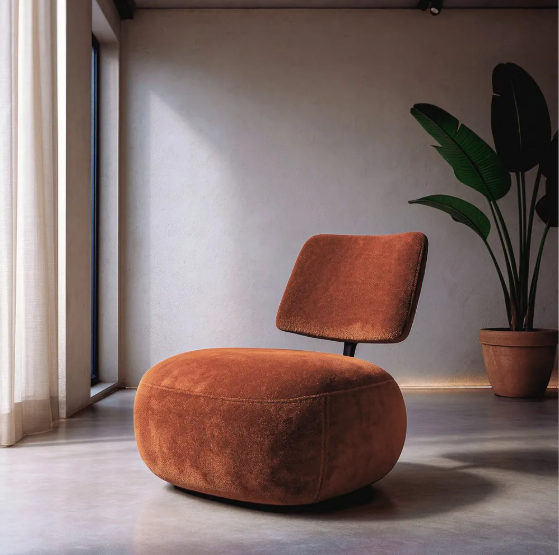 Sillón bajo color terracota tapizado en tejido sobre suelo de cemento con fondo claro y planta decorativa