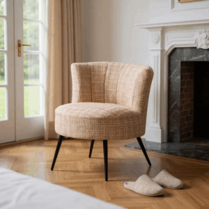 Sillón tapizado jaspeado en tonos beige con patas metálicas negras junto a una chimenea y ventana
