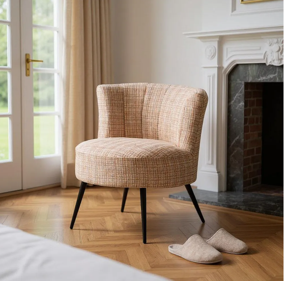 Sillón tapizado jaspeado en tonos beige con patas metálicas negras junto a una chimenea y ventana