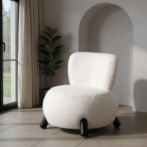 Sillón tapizado blanco con patas negras sobre suelo claro junto a ventana y planta decorativa