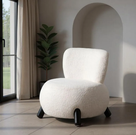 Sillón tapizado blanco con patas negras sobre suelo claro junto a ventana y planta decorativa