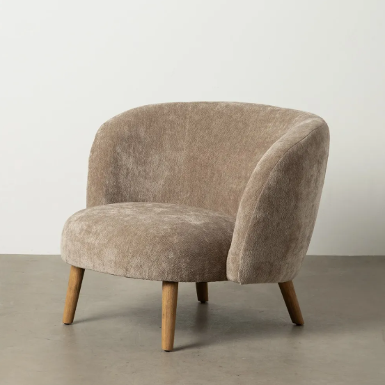 Sillón tapizado color taupe con estructura curva y patas de madera sobre suelo gris