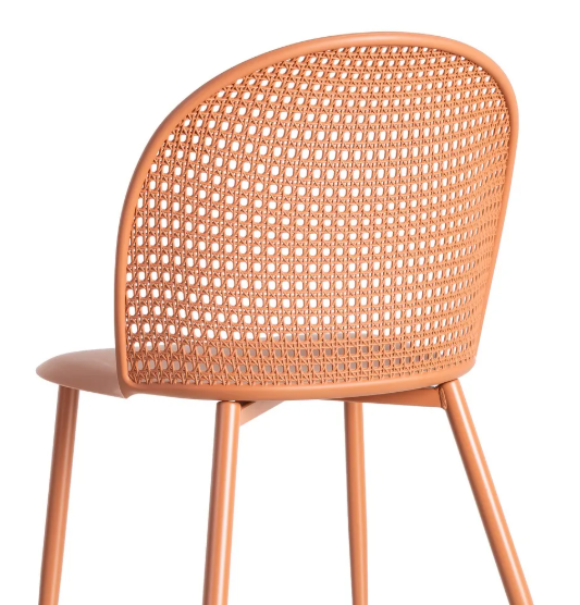 Silla color teja fabricada en polipropileno con respaldo calado y patas metálicas sobre fondo blanco