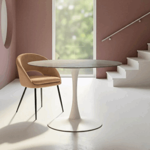 Mesa de comedor redonda con tablero de piedra sinterizada gris y base blanca, acompañada de una silla tapizada en un ambiente moderno con luz natural.