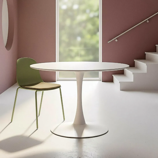 Mesa de comedor redonda color blanco con base metálica blanca, acompañada de una silla verde en ambiente moderno con pared rosada y luz natural.