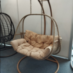 Sillón colgante de ratán sintético beige en exposición con cojines incluidos