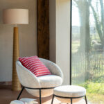 Sillón moderno tapizado en tela con patas metálicas negras, diseño envolvente disponible en gris, beige y rosa pastel.