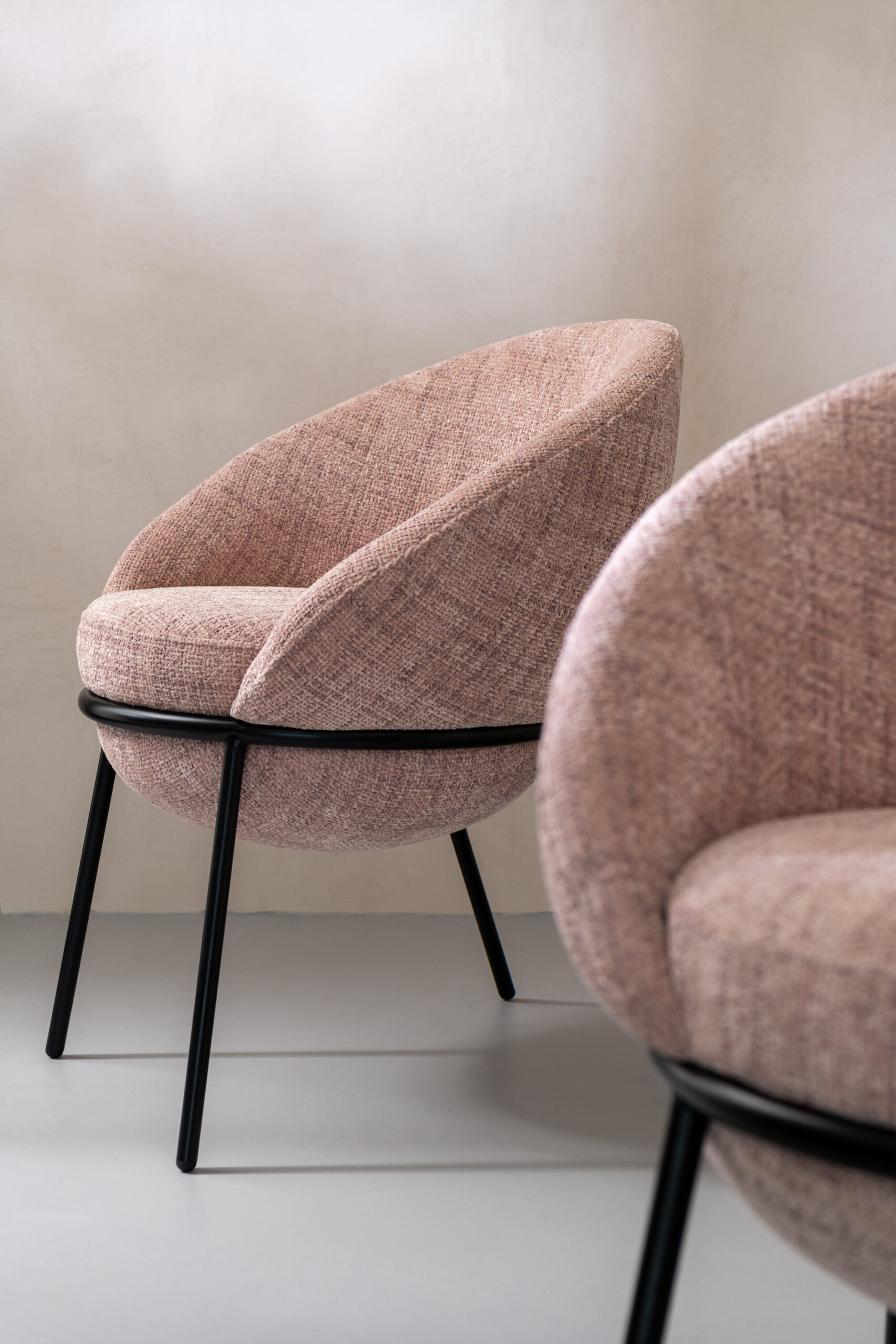 Sillón moderno tapizado en tela con reposapiés a juego y patas metálicas negras, disponible en gris, beige y rosa pastel.