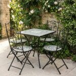 Conjunto de jardín compuesto por mesa redonda y dos sillas plegables de estructura metálica negra con asiento y tablero de mosaico decorativo, ideal para terraza o patio exterior.